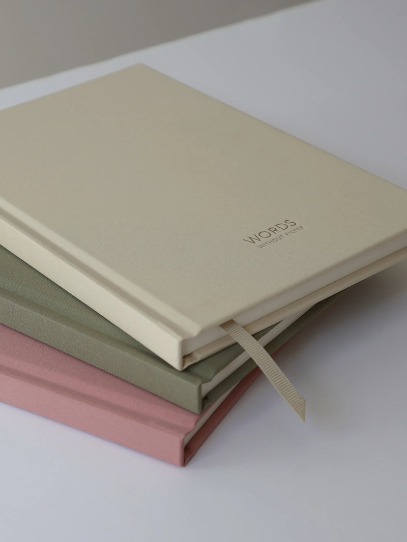 Three hardcover memory books stacked on a white surface, with the top book in cream-colored paper and the visible titles 'WORDS memory books
